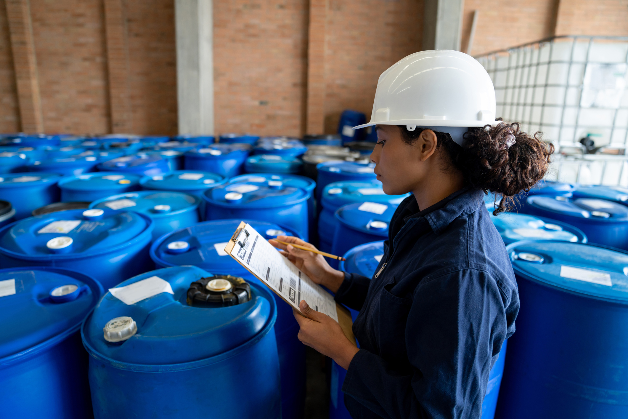 African American female chemical plant worker doing a stock inventory of barrels at a distribution warehouse