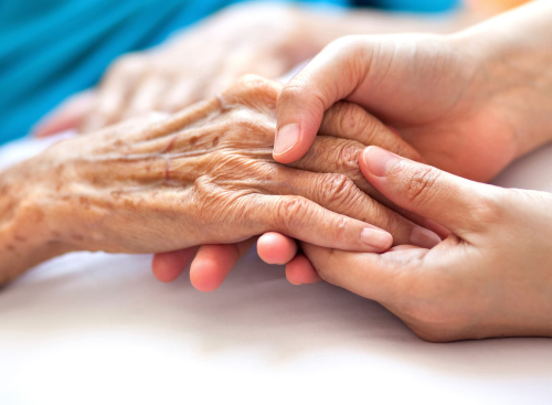 younger hands holding older hands of a loved one in longterm care