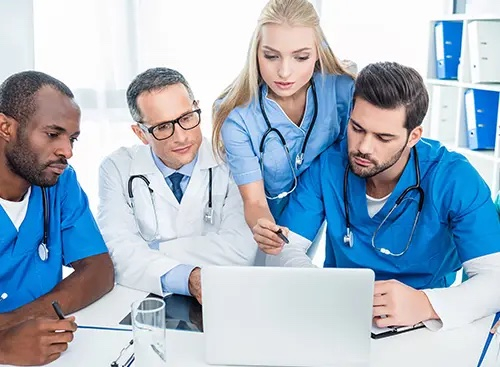 three male doctors and one female doctor looking at a laptop screen