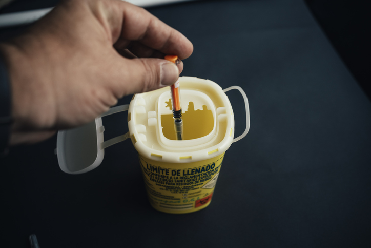 A person throwing a syringe into a small medical waste container