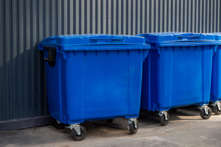 Two large blue plastic waste containers positioned near industrial wall outdoors