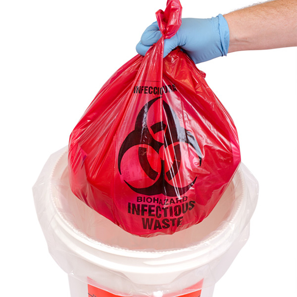gloved hand putting a red biohazard infectious waste bag into a pail