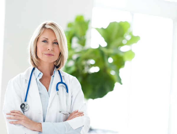 a female doctor posing with her arms crossed in a white coat with a blue stethoscope around her neck